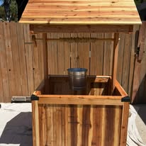 Wishing well with an open plank roof and galvanized bucket hanging above the empty planter box.