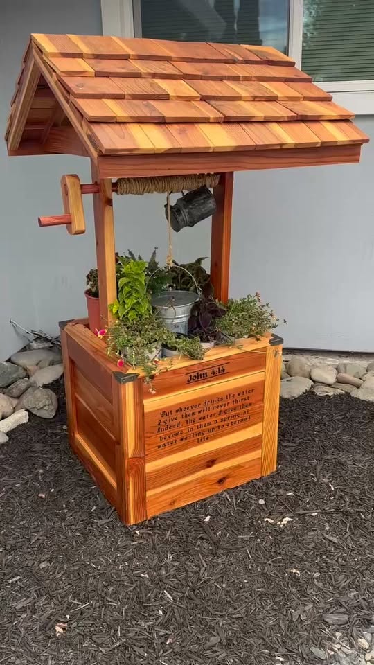 Redwood wishing well with a hand-laid shingle roof, rope crank and engraved John 4:14 panel, planted with ferns and herbs.